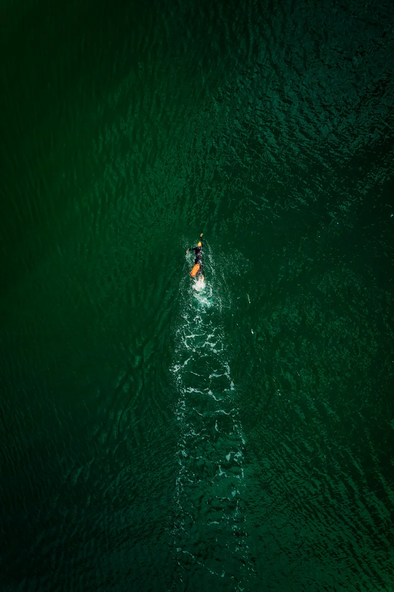 An open-water swimmer photographed from above, alone in dark water