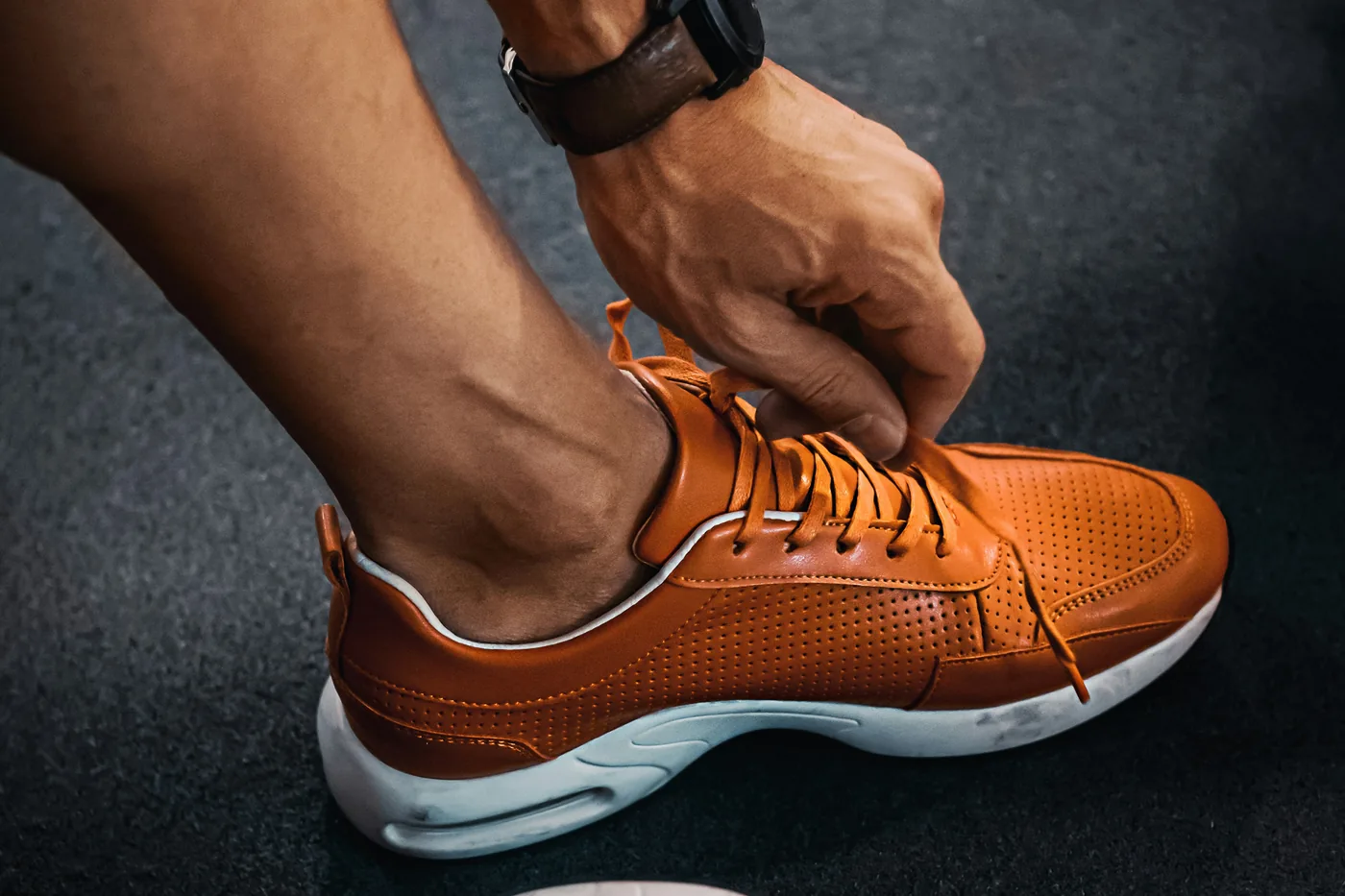 A runner tightening a shoe, a watch on the wrist